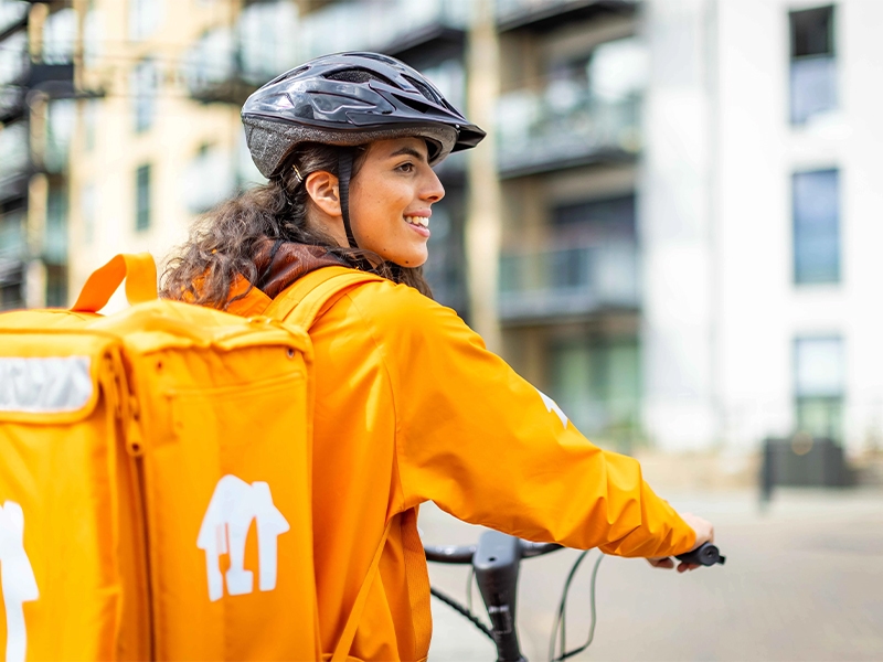 Een fietsbezorger met een oranje bezorgtas kijkt om in de stad